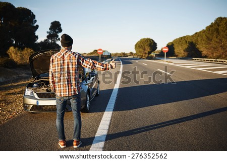Caucasian man trying stop cars in travel because his car broken down. Young man stand on freeway and shows thumbs up. Young interracial man in their twenties.