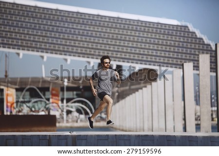 Running athlete man. Male runner sprinting during outdoors training. Athletic fit young sport fitness model in his twenties in full body length on road outside in city urban
