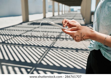 Unrecognizable close up portrait of young fitness asian woman in sportswear listening music with headphones an tablet after training outdoors at beautiful sunny day.