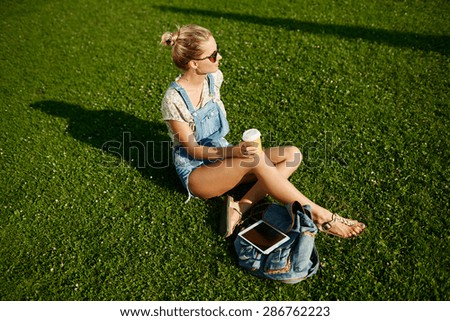 Young happy girl drinks coffee outdoor sitting on grass and smiling.