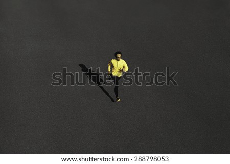 Top view runner man running sprinting for success on run at black road in yellow sportswear. Muscular fit sport model sprinter exercising sprint on city road. Full body length of Caucasian model.