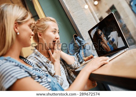 Portrait of beautiful girl blonde and charming Asian girl sitting in cafe and watching photos on laptop which they did on vacation.