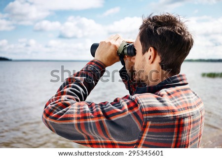 Close up back portrait man looks through binoculars while fishing at the lake on vacation