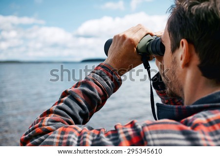 Close up back portrait man looks through binoculars while fishing at the lake on vacation