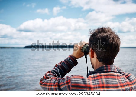 Close up back portrait man looks through binoculars while fishing at the lake on vacation