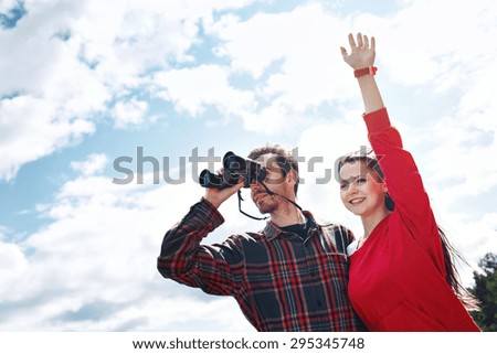 portrait of couple looks through binoculars while fishing on vacation with lake in background