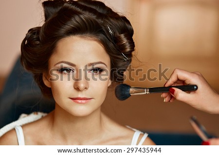 Beauty portrait of a young and attractive woman smiling and applying powder make up cosmetics with a brush.