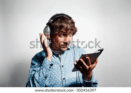 Closeup portrait surprised funny looking young hipster man holding tablet pc, reading bad news on digital tablet and listening music on headphones. Face expression, emotion