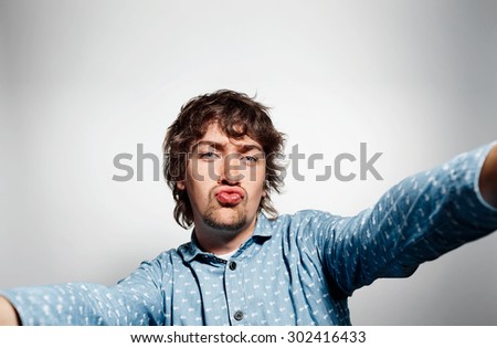 Close up portrait of a young kissing man holding a smartphone digital camera with his hands and taking a selfie self portrait of himself standing against grey background