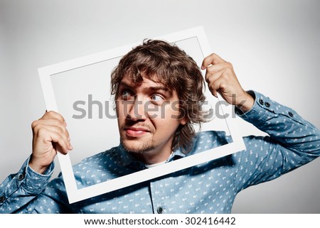 Closeup portrait businessman executive looking sideways, curious surprised confused through white picture frame thinking beyond borders accepted rules isolated grey background. Face expression emotion