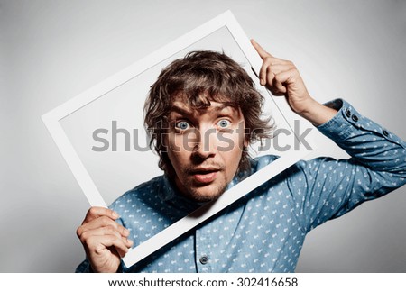Closeup portrait young man executive looking surprised, curious surprised confused through white picture frame thinking beyond borders accepted rules isolated grey background. Face expression emotion