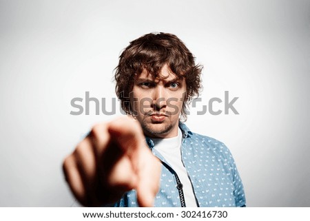 Closeup portrait angry young business man, guy, mad worker, pointing his finger against somebody at isolated grey background. Negative emotions, facial expression