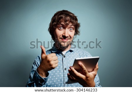 Closeup portrait handsome young smiling business man, corporate employee giving thumbs up sign at camera with tablet pc at grey background. Positive human emotions, facial expression, feelings.