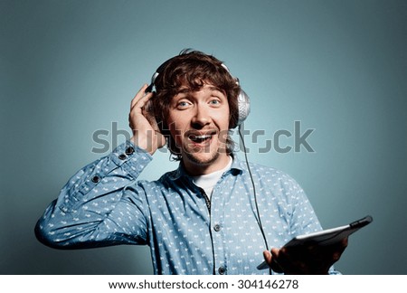 Closeup portrait surprised funny looking young hipster man holding tablet pc, reading bad news on digital tablet and listening music on headphones. Face expression, emotion