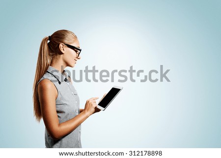 Closeup portrait of happy young blonde business woman using tablet pc isolated on blue background. Side view of a smiling girl holding a digital tablet computer.