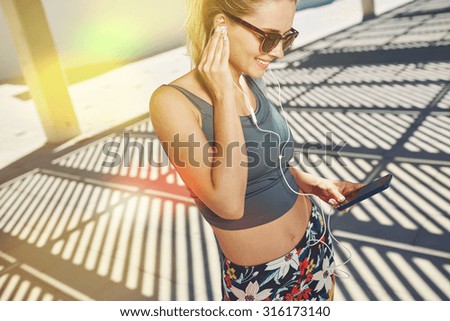 Close up portrait of young fitness blonde woman in sportswear listening music with headphones after training outdoors at beautiful sunny day.