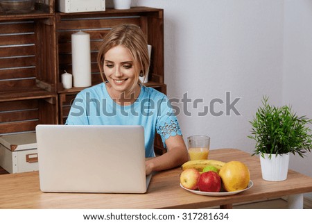 Young blonde woman looking for a recipe information on laptop computer in the home kitchen. Dieting Concept.