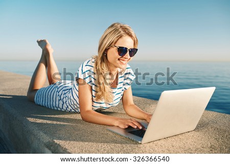 Woman on the beach browsing social media on a computer in summer with the sea in the background