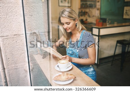 Closeup portrait of cafecity lifestyle woman sitting in trendy urban cafe reading magazine and drinking coffee with a croissant during your vacation