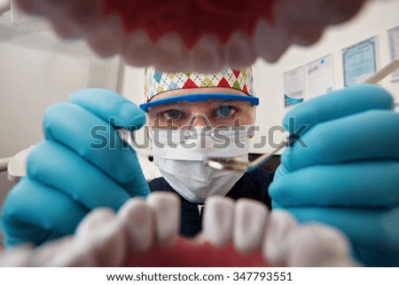 Healthy teeth and smile. Serious doctor directly into the camera. Dentist sitting in the dentist for dental chair and holding a dental drill in hand.