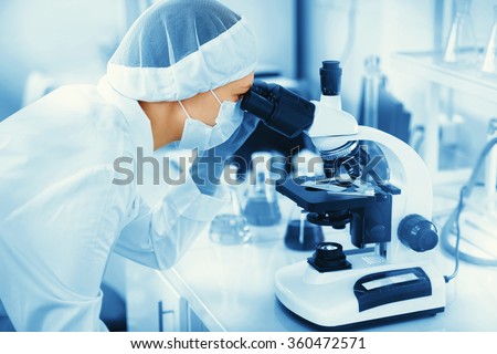 Young woman medical researcher looking through microscop slide in the life science (forensics, microbiology, biochemistry, genetics, oncology) laboratory. Medicine concept.