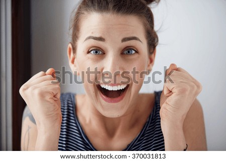 Surprised woman with hands up amazed or shocked by unexpected news holding close palms up and showing happy expression. Young adult woman on greybackground