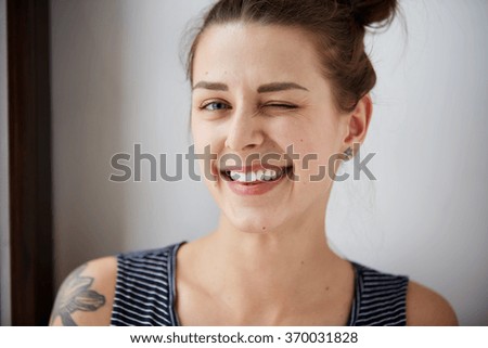 Portrait of attractive cute woman winking over gray background. Looking at the camera. Positive human emotion facial expression body language. Funny girl