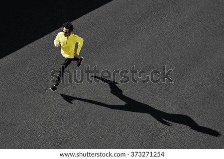 Running man sprinting for success on run. Top view athlete runner training at fast speed at asphalt. Muscular fit sport model sprinter exercising sprint in yellow sportswear. Caucasian fitness model