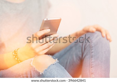 Beautiful hipster woman checking email via mobile phone while grey wall, charming female holding cell telephone in hands while waiting for friends.