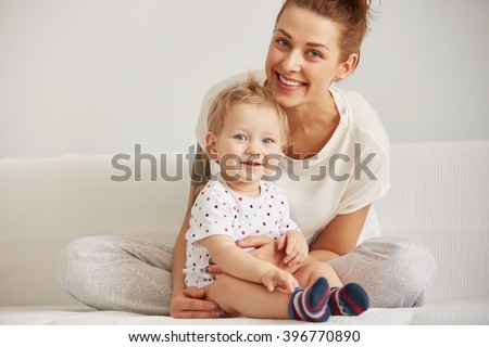 Young mother with her one years old little son dressed in pajamas are relaxing and playing in the bedroom at the weekend together, lazy morning, warm and cozy scene. Selective focus.