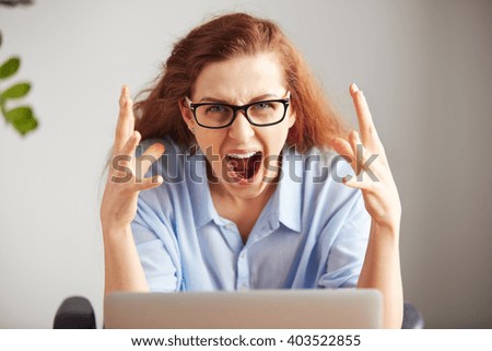 Portrait of a young attractive businesswoman with frustrated look working on laptop at  office. Outraged screaming freelance student looking at camera with desperate expression: I hate this computer