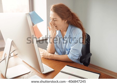 Portrait of tired sleepy businesswoman yawning, working at desk in the office in front of computer. Bored young female freelancer working on PC at home. Overwork and sleep deprivation concept