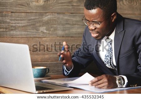 Disappointed African businessman is dazed and confused by a mistake in official documents. His bewilderment makes his eyebrows frowned and face unhappy. He feels total disagreement about the deal.