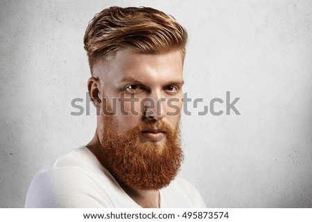 Sideways portrait of natural blond Caucasian man on white background. Bearded hipster with clean shaved temples and stylish well-trimmed moustaches looking serious and brutal with long facial hear.