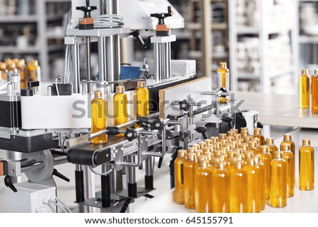 Cosmetics factory. Bottling line filled with yellow shampoo. Automated process on factory. Line of bottles filled with yellow substance going on conveyor to be twisted. Research, innovation, creation