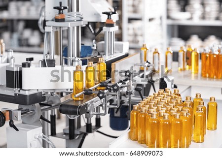 Horizontal shot of cosmetics or pharmacy plant with automated equipment. Transparent plastic bottles filled with yellow substance standing on desk and conveyor line, ready for transportation