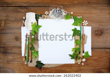 Artistic spring time composition with green leaves and a heart next to shredded paper and daisy flowers over white and brown background placeholder paper on vintage weathered wood