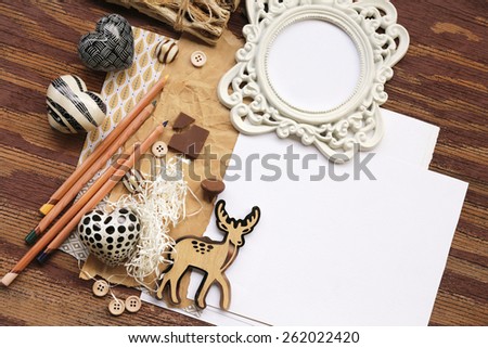 Rustic nature composition with baby deer placed over shredded paper next to pencils and artistic white photo frame with buttons over brown and white placeholder paper on the right and vintage wood