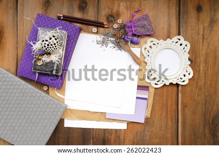 Artistic composition with lavender seeds and flowers next to a purple diary notepad placed next to a rounded photo frame and notebooks over white and brown sheets of paper and weathered, vintage wood