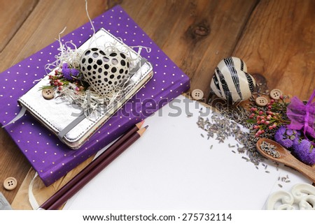Rustic composition with a purple diary notepad under a white book and heart and an organza bag filled with lavender seeds and flowers next to a white placeholder sheet of paper over brown vintage wood