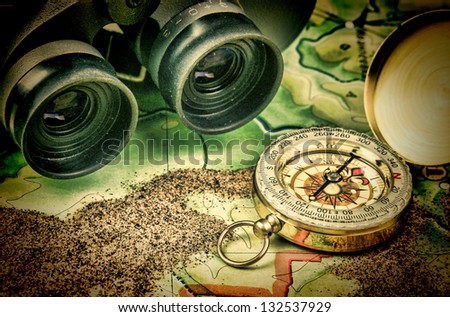 binoculars and a compass on the map with sand