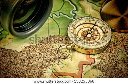 Old binoculars and a compass on the map with sand