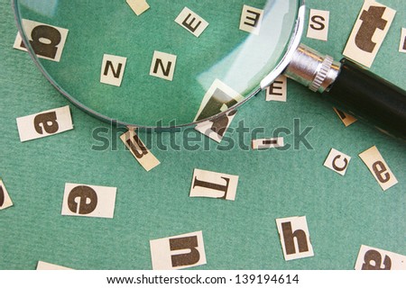 letters cut from newspaper and magnifying glass on green background
