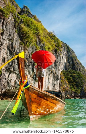 young girl standing in a wooden boat with a red umbrella in the Gulf of Phi Phi Don Thailand