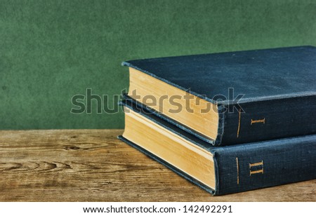 Old books on a wooden shelf against a green wall