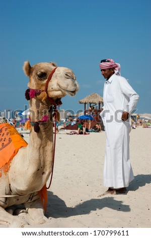 DUBAI, UAE - NOVEMBER 16, 2012: Arab man and camel on Jumeirah Beach in Dubai at the Burj Al Arab background.  Dubai was the fastest developing city in the world between 2002 and 2008.