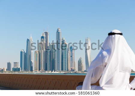 DUBAI, UAE - NOVEMBER 7: Modern buildings in Dubai Marina,, UAE. In the city of artificial channel length of 3 kilometers along the Persian Gulf. Man in Arab dress looks at the city