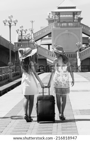 Two young girls walk along the road with a suitcase