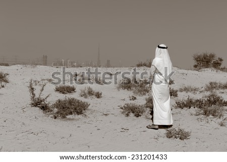 Arab man in national dress stands in the desert and looks at the city of Dubai. Toned.