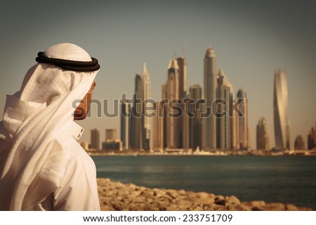 DUBAI, UAE - NOVEMBER 7: Modern buildings in Dubai Marina,, UAE. In the city of artificial channel length of 3 kilometers along the Persian Gulf. Man in Arab dress looks at the city. Toned
